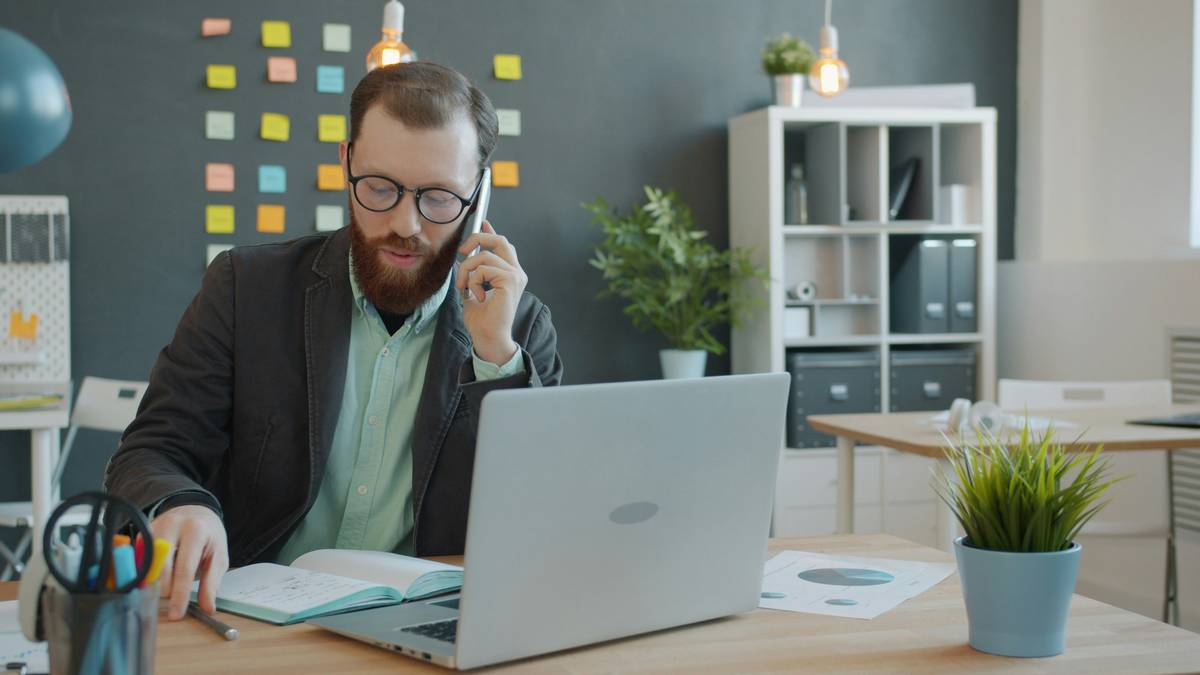 business phone etiquette illustrated with a professional answering a desk phone while smiling, headset on, notes organized